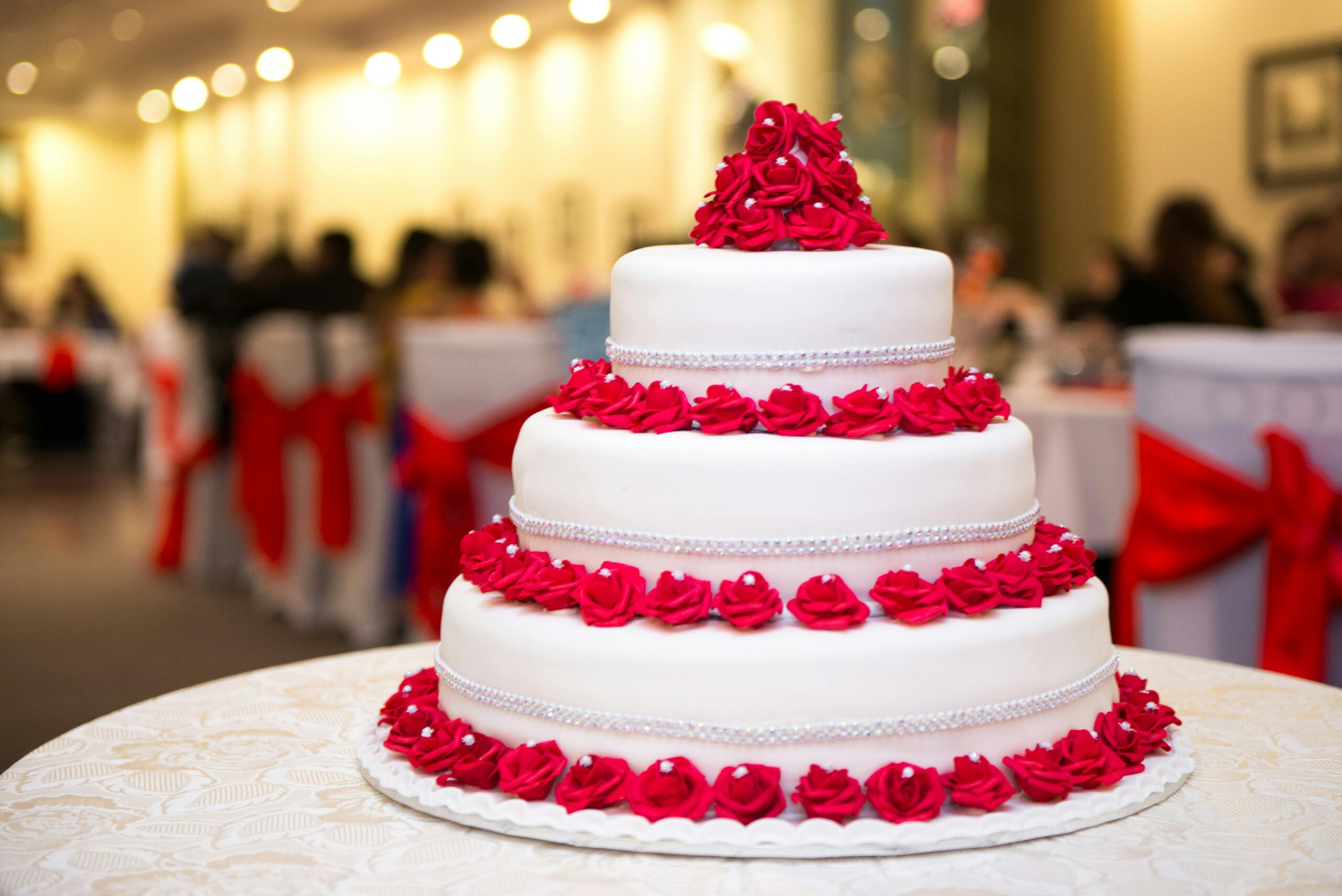 A stunning three-tier wedding cake adorned with vibrant red roses at a formal reception.