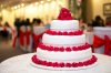 A stunning three-tier wedding cake adorned with vibrant red roses at a formal reception.